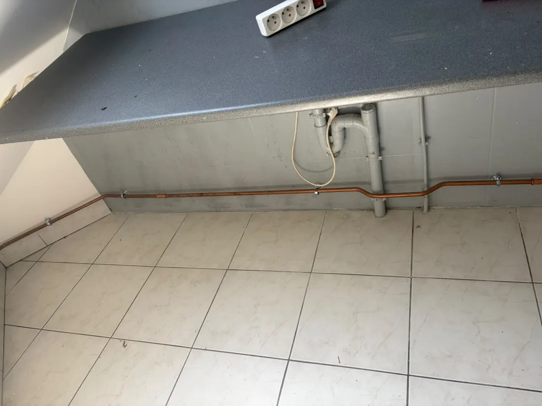 Tube cuivre neuf fixé sur colliers le long du mur, sous un plan de travail