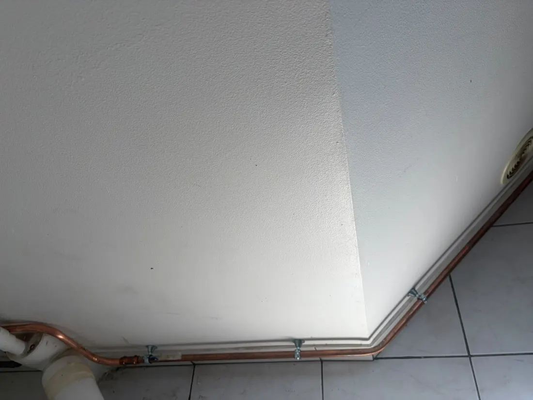 Réseau d'eau froide en cuivre passé en haut de mur et contournant l'angle du plafond