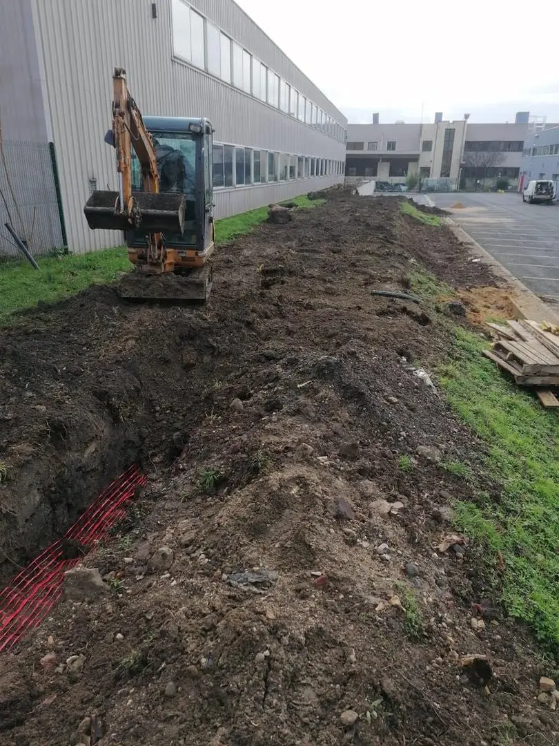 Mini-pelle en cours de terrassement le long d'un bâtiment professionnel